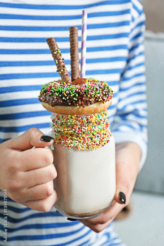 Girl holding milkshake with donut and other sweets in jar