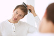 © Africa Studio - Handsome young man combing hair while standing in front of mirror