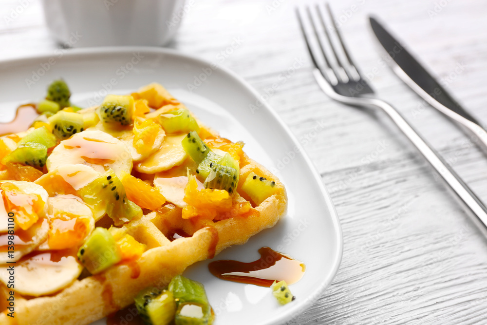 Delicious waffle with fruits and syrup on white plate