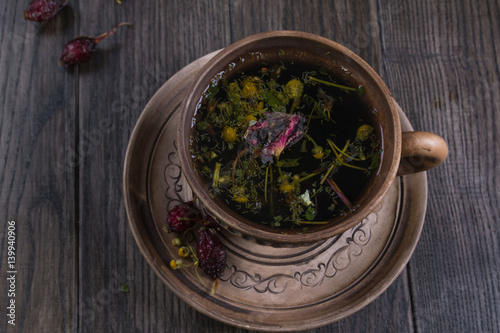 Fototapeta na drzwi i meble Herbal tea, herbs and flowers in a clay cup on wooden table
