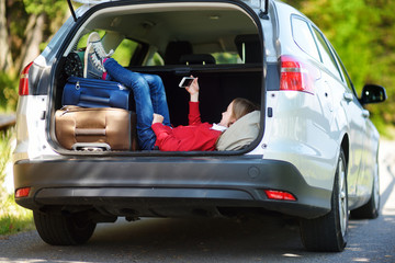 Wall Mural - Adorable little girl ready to go on vacations with her parents. Kid playing with her phone in a car.