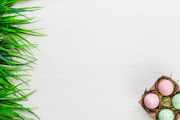 Easter spring colorful eggs and green grass lying on white wooden table background