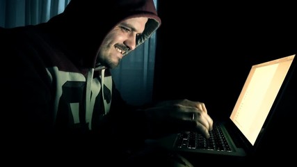 Wall Mural - male hacker in a hood works on a computer