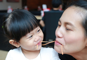 Funny kid girl eating carrot with mother.