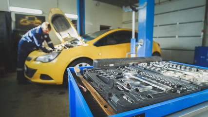 Defocused - a worker mechanic checks the electrical in the hood of the yellow car, garage workshop