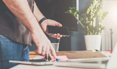 Wall Mural - Businessman standing in an office near the table, leafing through a catalog and holding a smartphone.