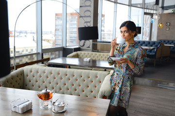 Wall Mural - a beautiful woman stands at a table in a cafe with a Cup in hand