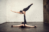 Young athletic couple practicing acroyoga. Balancing in pair. Fit active  pair yoga time. Sporty handsome man supporting and holding slim beautiful  brunette woman. Training time. Asana Stock Photo