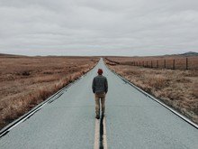 Man Standing In Middle Of Road By Fields, Rear View 