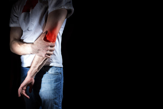 Fototapete - man, holding her painful  elbow, arm, experiencing pain,  red spot, on the black background, Sport injury