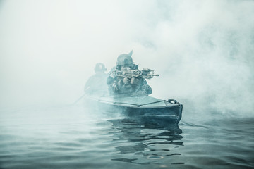 Special forces marine operators in camouflage uniforms paddling army kayak through river fog. Diversionary mission, machine gunner ahead