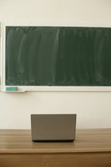 Wall Mural - Laptop on a table, blackboard in background