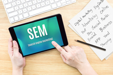 Poster - Hand using tablet with SEM (Search engine marketing ) word on screen with list of digital marketing features on paper on work table,Online business concept