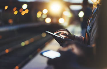 Enjoying travel. woman waiting on station platform on background light electric moving train using smart phone in night. Tourist texting message and plan route of stop railway, railroad transport