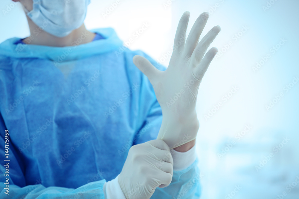 Young doctor putting on rubber gloves in clinic, closeup