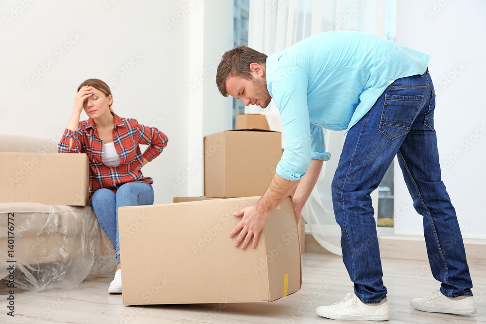 Couple suffering from ache while moving boxes in room