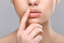 Woman With Cold Sore Touching Lips On Light Background