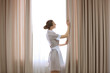 Hotel service concept. Chambermaid adjusting curtains in the room