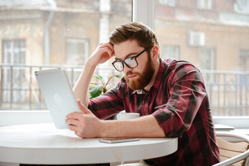 Sticker - Concentrated bearded young man using tablet computer.