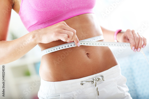 Fotografie, Obraz Slim young woman measuring her waist with a tape measure