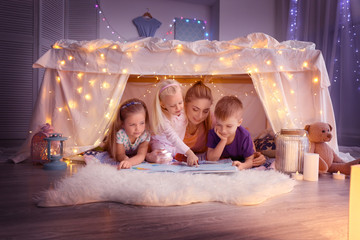 Wall Mural - Young woman and cute children reading book in hovel at home