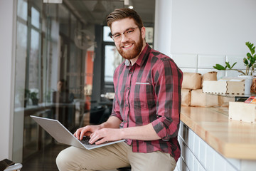 Sticker - Smiling bearded young man in glasses using laptop