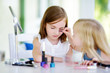 © MNStudio - Two cute funny sisters applying make-up on sunny summer day at home