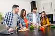 © W PRODUCTION - group of friends, four people man and woman at home cooking, drinking wine and preparing food meal together in the kitchen