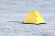 Fisherman tent from yellow with black bottom in snow on frozen river in winter day closeup