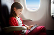 © MNStudio - Adorable little girl traveling by an airplane. Child sitting by aircraft window and using a digital tablet