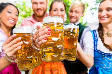 Freunde, zwei Männer, drei Frauen, stehen im Biergarten mit Maßkrügen