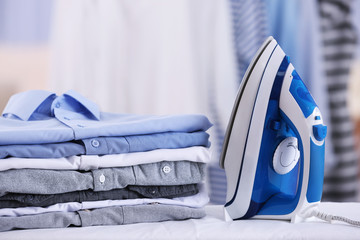 Wall Mural - Electric iron and pile of clothes on blurred background