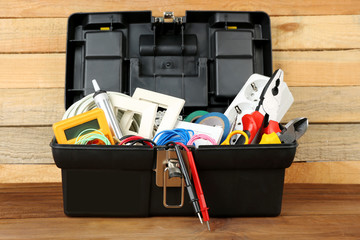 Box with electrician tools on wooden background