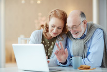 Portrait Of Beautiful Elderly Couple Waving To Laptop Camera Saying Hello Video Chatting With Family Using Modern Laptop And Smiling Happily