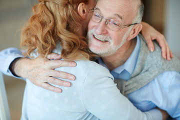 Portrait of loving mature people embracing happily celebrating holiday together at home, woman hugging gray haired man smiling with joy