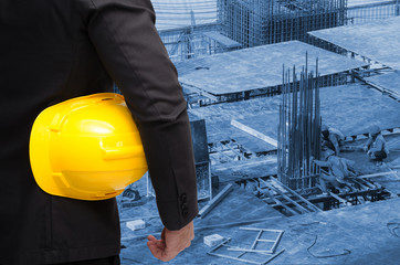 Wall Mural - double exposure of businessman hold in hand yellow safety helmet  industrial concept on blurred construction site workers background, color tone effect.