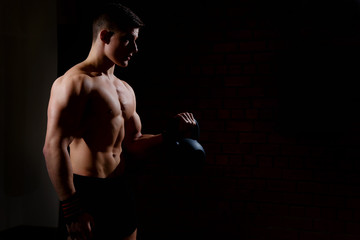 Wall Mural - Silhouette of a young man doing weight exercises with a dumbbell on a dark background. Bodybuilder does a heavy weight training for the biceps. Free space for text.