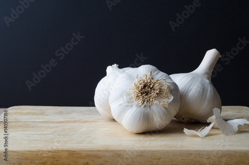 Fotografía Garlic Bulbs Grouped on Chopping Board with Black Background