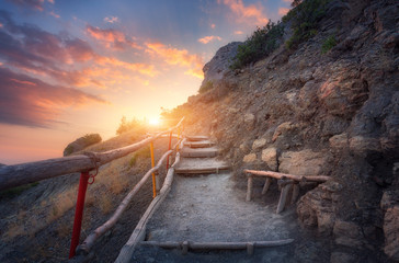 Wall Mural - Stone stairs with wooden railing in the mountains at sunset. Landscape with mountain path and rocks against colorful blue sky with clouds and orange sunlight. Trail leading to the mountain peak