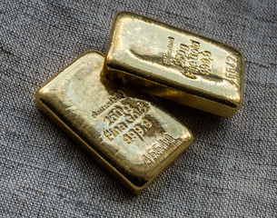 Two cast gold bars weighing 250 grams against the background of the texture of coarse cloth.