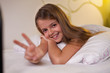 Young girl showing victory sign lying in bed, shallow depth
