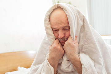 Sad elderly man suffers from insomnia. He covered himself with a blanket to make it easier to fall asleep and it was not cold.