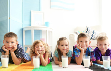 Wall Mural - Cheerful children with glasses of milk lying on colourful carpet in the room