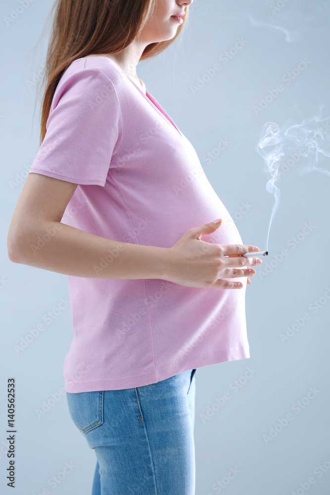 Pregnant woman smoking cigarette on grey background Stock Photo