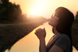 Woman praying with hands together on nature sunset background