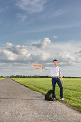 Wall Mural - Full length of young man holding anywhere sign on empty road