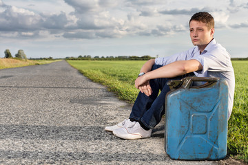 Wall Mural - Full length of young man with empty gas can sitting by road