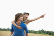 © MDBPIXS - Happy woman showing something while enjoying piggyback ride on man in field