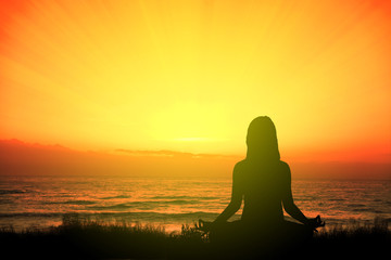 Girl doing yoga meditating in the beach sitting on the grass at sunset. Empty copy space for Editor's text.