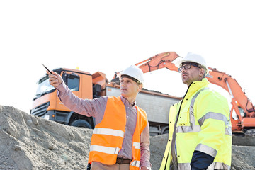 Wall Mural - Engineer showing something to colleague while discussing at construction site against clear sky